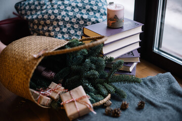 Fresh spruce in a wicker basket with wrapped gifts and pile of books on the background, indoor cozy view