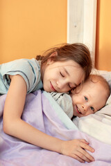 Sister and little brother baby are lying on the bed at home in the room and hugging fun.