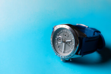 Reloj de pulsera plateado con correa azul sobre fondo azul cielo, con espacio para texto....