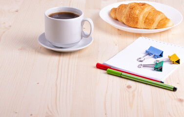 a white ceramic cup with black espresso, french croissant as breakfast or snack concept on rustic, natural texture wooden surface