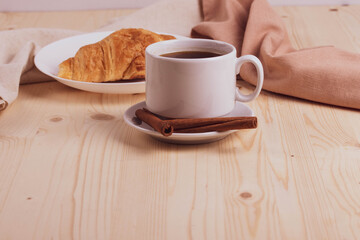 a white ceramic cup with black espresso, french croissant as breakfast or snack concept on rustic, natural texture wooden surface