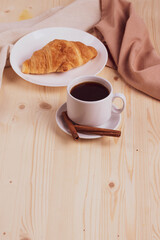 a white ceramic cup with black espresso, french croissant as breakfast or snack concept on rustic, natural texture wooden surface