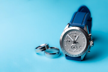 Reloj de pulsera plateado con correa azul sobre fondo azul cielo y anillos desenfocados con espacio para texto. Accesorios para hombre.