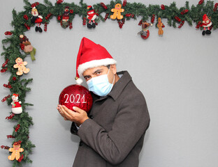 latin man with protection mask, santa claus hat and red sphere,
Christmas decoration, new normal...