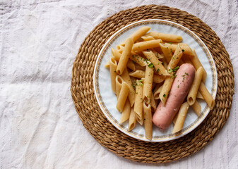 Boiled macaroni with meat sausage in a plate and sprinkled with spices on top.