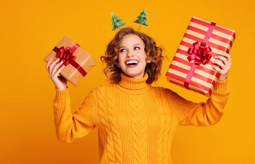 cheerful surprised   woman  laughs with her mouth open holds a Christmas gifts on a colored yellow background.