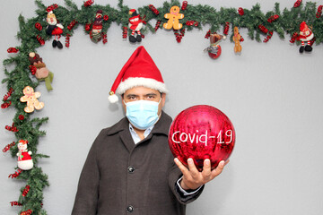 latin man with protection mask, santa claus hat and red sphere,
Christmas decoration, new normal...