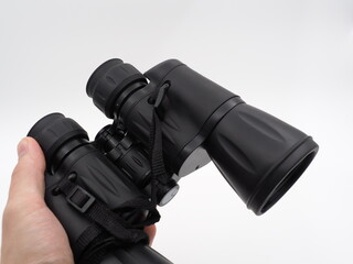 A man's hand holds a black tourist binoculars on a light background