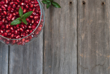 Fresh pomegranate arils with mint leaves in a glass bowl on a weathered board table top.