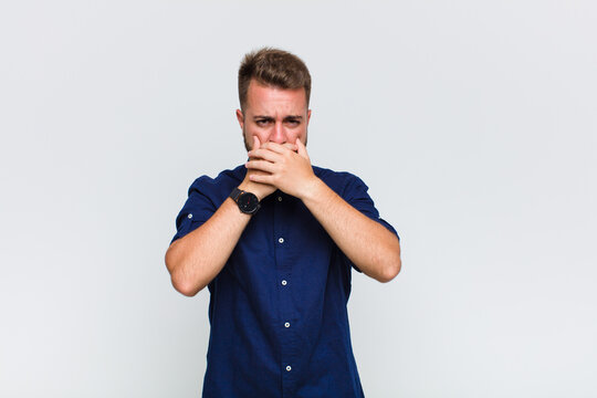 young man covering mouth with hands with a shocked, surprised expression, keeping a secret or saying oops