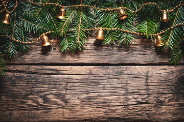 Christmas decoration background.Green fir branches and golden garland with bells on a rustic aged wooden wall. Space for copy.