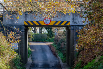 Portrait orientation of a front on view of a low railway bridge over a quiet rural road in the county of Norfolk