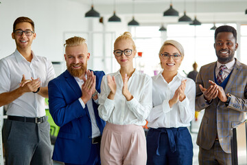 portrait of positive interracial team looking at camera in the office, posing, young people have a good cooperation, stand clapping hands celebrating congratulating