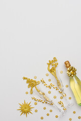 Festive white background with gold decoration , bottle of sparkling wine with two crystal glasses, shiny golden serpentine confetti and glittering snowflakes, copy space, top view