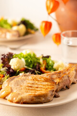 Fried pork entrecote on the bone with stewed pumpkin pieces and salad in a plate close up, green salad with cauliflower and napa cabbage, bell pepper and spices