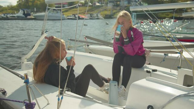 Two young athletes during a break in the regatta drink coffee and communicate on the Internet on smartphones. Slowmotion.