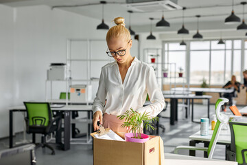 unhappy female employee packing things at work, she is fired from work, in the office