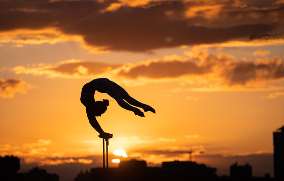 Flexible female circus Artis keep balance and doing contortion on the rooftop against dramatic sunset and cityscape. Handstand and equilibrium concept 