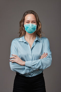 Retrato de mujer rubia empresaria de mediana edad con tapabocas o barbijo. Usa blusa celeste y esta sobre fondo gris.