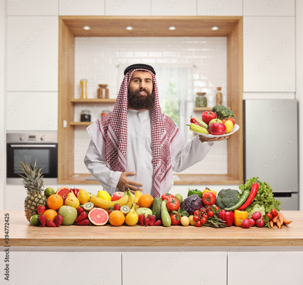 Wall mural traditional saudi arab man in a kitchen holding a plate of fruits and vegetables