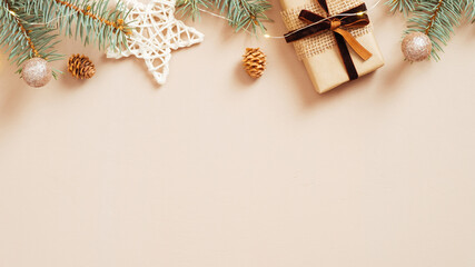Christmas frame top border made of fir tree branches, gift box, star, balls, garland on pastel beige background. Flat lay, top view. Xmas banner mockup with copy space