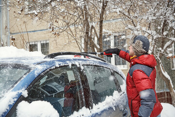 a man brushing the snow off the windshield of his car