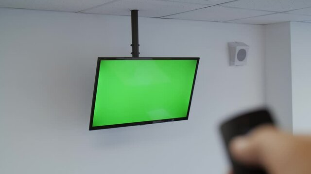 A male hand switches channels on a TV with a green screen