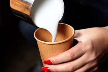 Pouring milk into a paper cup from a pitcher