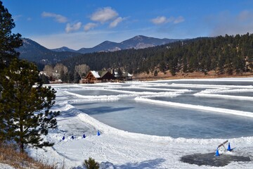 Ice skating on Evergreen Lake with a mountain view, blue sky and pines. Winter recreational scene in Colorado mountains.