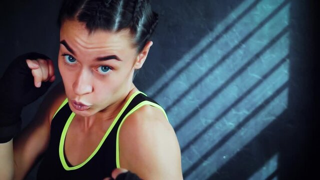 Female boxer with boxing wraps on fists looking at camera while practicing punches in slow motion. Fit woman working out in gym. Concept of sport