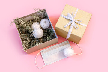 Fototapeta na wymiar Gift box with white balls, medical protective mask and branches of christmas tree on pink background. Christmas and New Year during pandemic of coronavirus infection. Flat lay, top view .