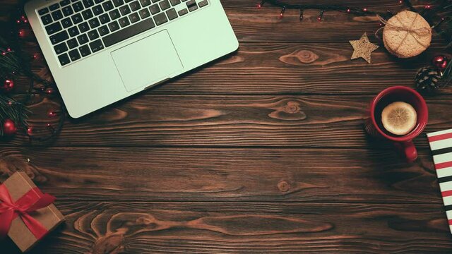 Layout of wooden table with laptop, tea with lemon, Christmas tree branches and garlands. New Year's atmosphere.