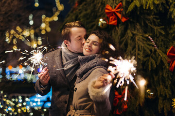 Couple in love having fun with sparklers on christmas decoration lights street. Romantic date for Valentine's day Outdoors. Young man and Woman laughing. Winter wonderland city  scene. New Year party