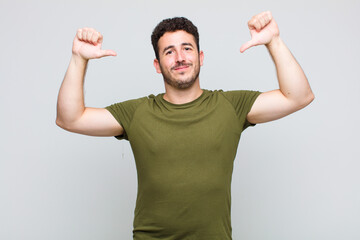 young man feeling proud, arrogant and confident, looking satisfied and successful, pointing to self