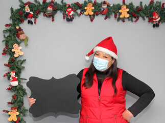 latin woman with protection mask, santa claus hat and blackboard for message.
Christmas decoration,...