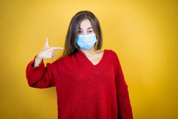 Young beautiful woman wearing red sweater over isolated yellow background pointing the mask. Warning expression with negative and serious gesture