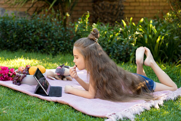 Little girl, schoolgirl looks in a laptop in the garden