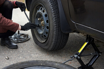 A woman removes the wheel with a key near her car with a flat tire.