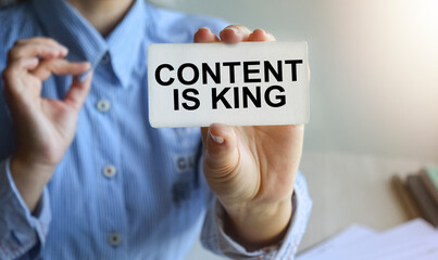 Business woman sitting at a table in a light office holding a business card. The content of the lettering has implications for business concept and marketing. Close-up, soft light.