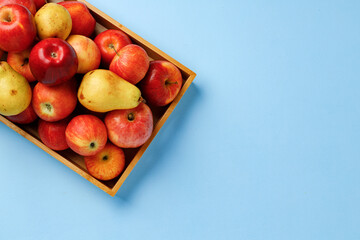 Wooden box with apples and pears on blue background