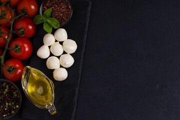 Ingredients for Italian caprese salad with mozzarella balls, tomatoes and spices, on a board. Top view