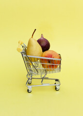 Shopping trolley with few fruits on pastel yellow background. Vertical shot, copy space. Shopping of vegetarian diet products. Trendy sale minimal concept.