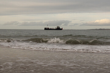 big splashing waves at the dutch coast and a boat and the sky in the background in winter