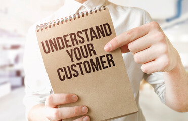 Text UNDERSTAND YOUR CUSTOMER on brown paper notepad in businessman hands in office. Business concept