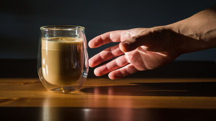 Male holds hand pglass cup with coffee on dark background