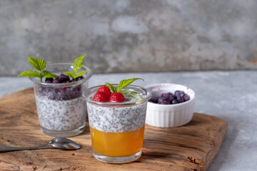 Dessert with chia seeds and berries in glass glasses on a wooden board on a gray background. Superfoods and healthy lifestyle concept.