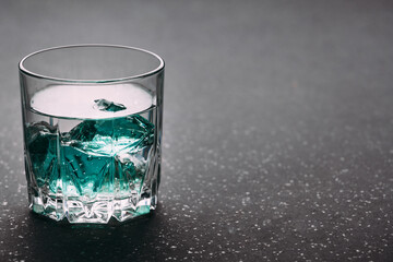 Gin in a glass on a black background with blue ice cubes on a wooden surface. Alcohol with ice. Place for an inscription..