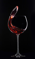 Large glass with red wine on a black background. Splashes of wine..