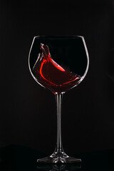 Large glass with red wine on a black background. Splashes of wine..