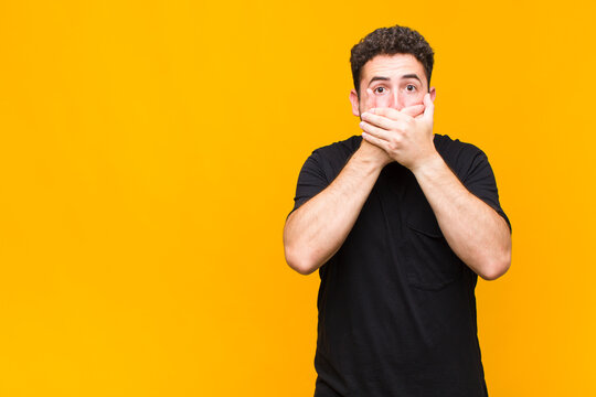 young man covering mouth with hands with a shocked, surprised expression, keeping a secret or saying oops